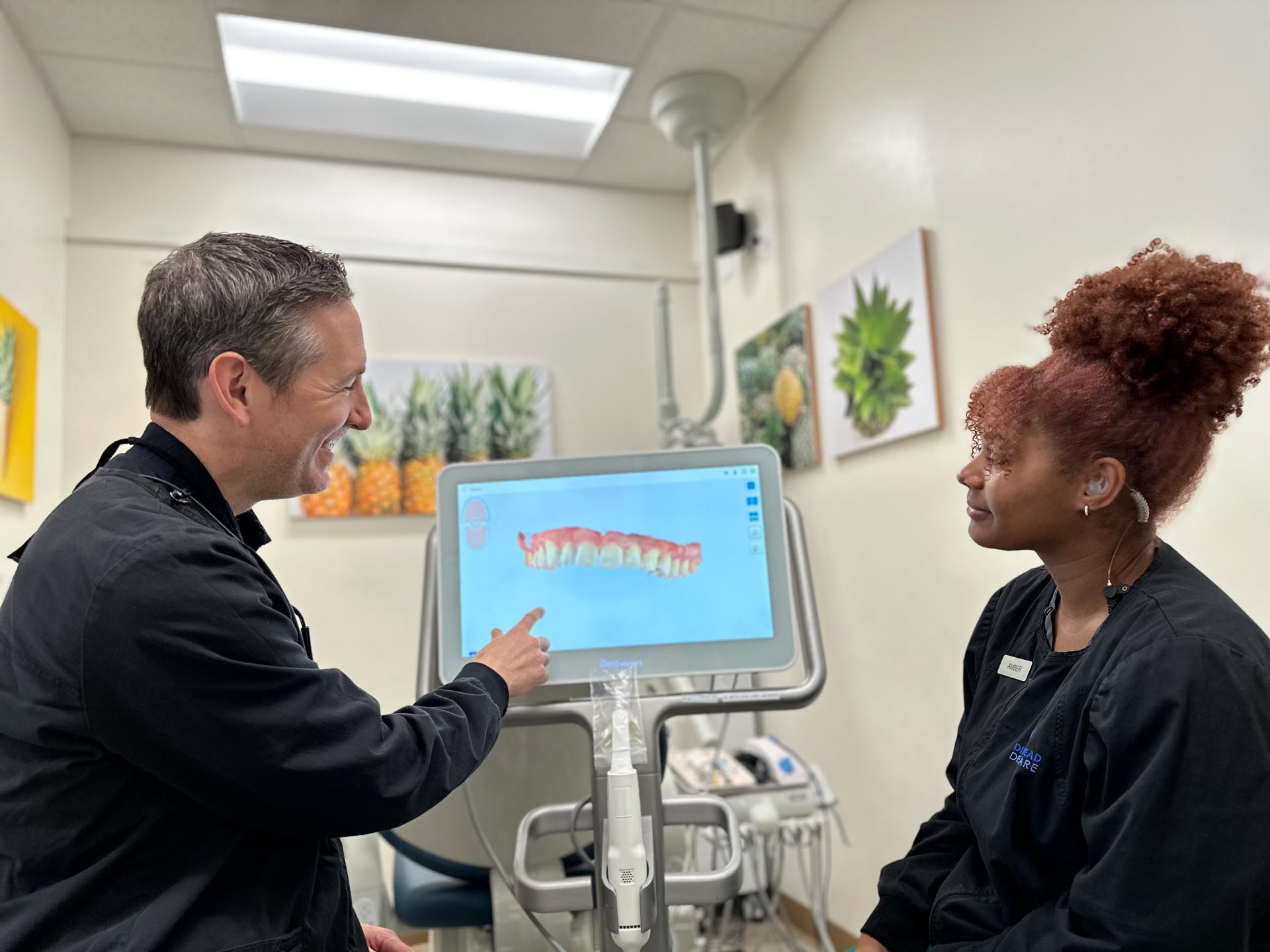 A man and two women are standing in front of a medical device with screens displaying dental images, likely discussing oral health care.