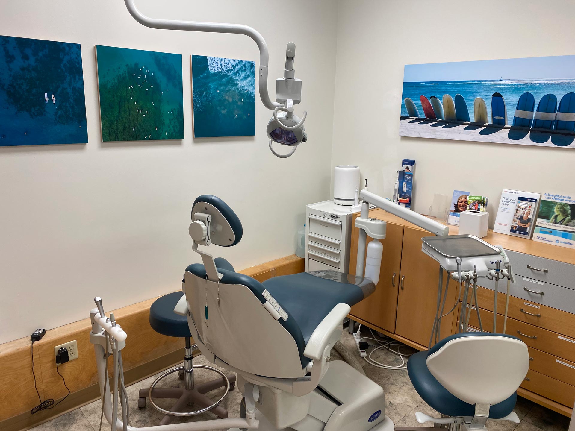 The image shows an interior view of a dental office with a modern dental chair, a dental mirror, and various pieces of equipment typically found in a dental practice.