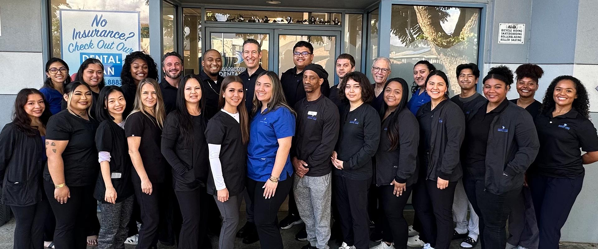 This is a photograph of a group of people posing together outside a building with a sign that reads NO ENTRANCE.