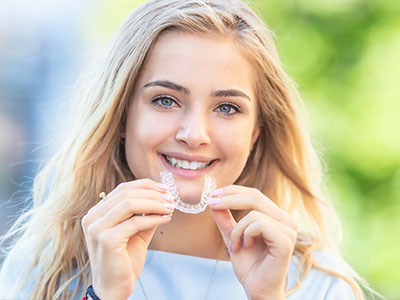 A young woman with a radiant smile holding up a dental retainer, smiling broadly at the camera.