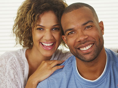 This image depicts a man and a woman posing closely together with smiles on their faces, likely a couple sharing a moment of happiness.