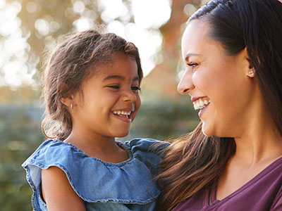 A woman and child are smiling at each other outdoors during daylight hours.