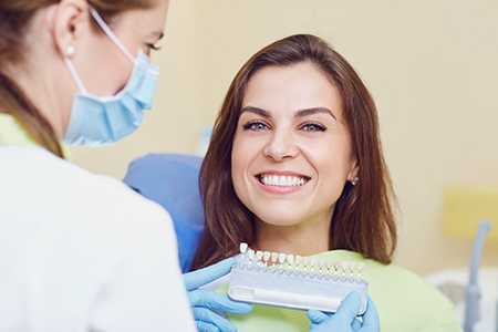 A dental hygienist is smiling at a patient with a dental device, both wearing face masks and gloves, in an indoor setting.
