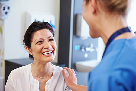 A woman with a smile sits next to a medical professional in a hospital setting, engaging in a conversation.