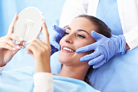 A woman sitting on a dentist s chair with a mirror placed over her eyes, receiving dental care from a professional wearing gloves.