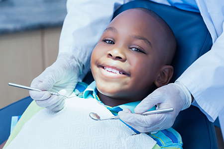 The image shows a young boy sitting in a dental chair with a broad smile, receiving dental care from a dentist who appears to be adjusting his mouthguard.