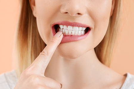 A woman with her finger on her teeth, possibly in the process of brushing them or showing off a dental product, against a bright background.