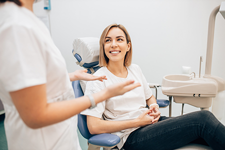A woman sitting in a dental chair with a smile on her face, being attended to by two dental professionals.
